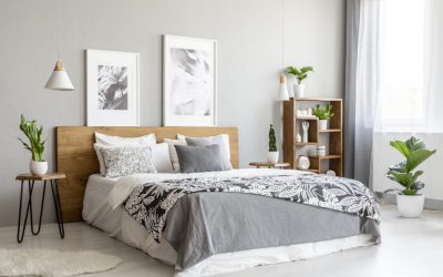 Patterned blanket on wooden bed in grey bedroom interior with plants and posters. Real photo